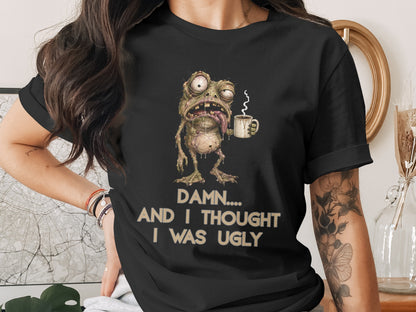 Black t-shirt with illustration of a drooling frog holding coffee mug and text "DAMN... AND I THOUGHT I WAS UGLY".