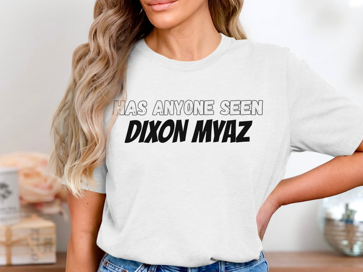 White t-shirt with text "HAS ANYONE SEEN DIXON MYAZ" in black and grey.
