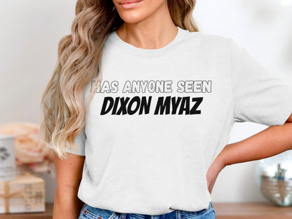 White t-shirt with text "HAS ANYONE SEEN DIXON MYAZ" in black and grey.
