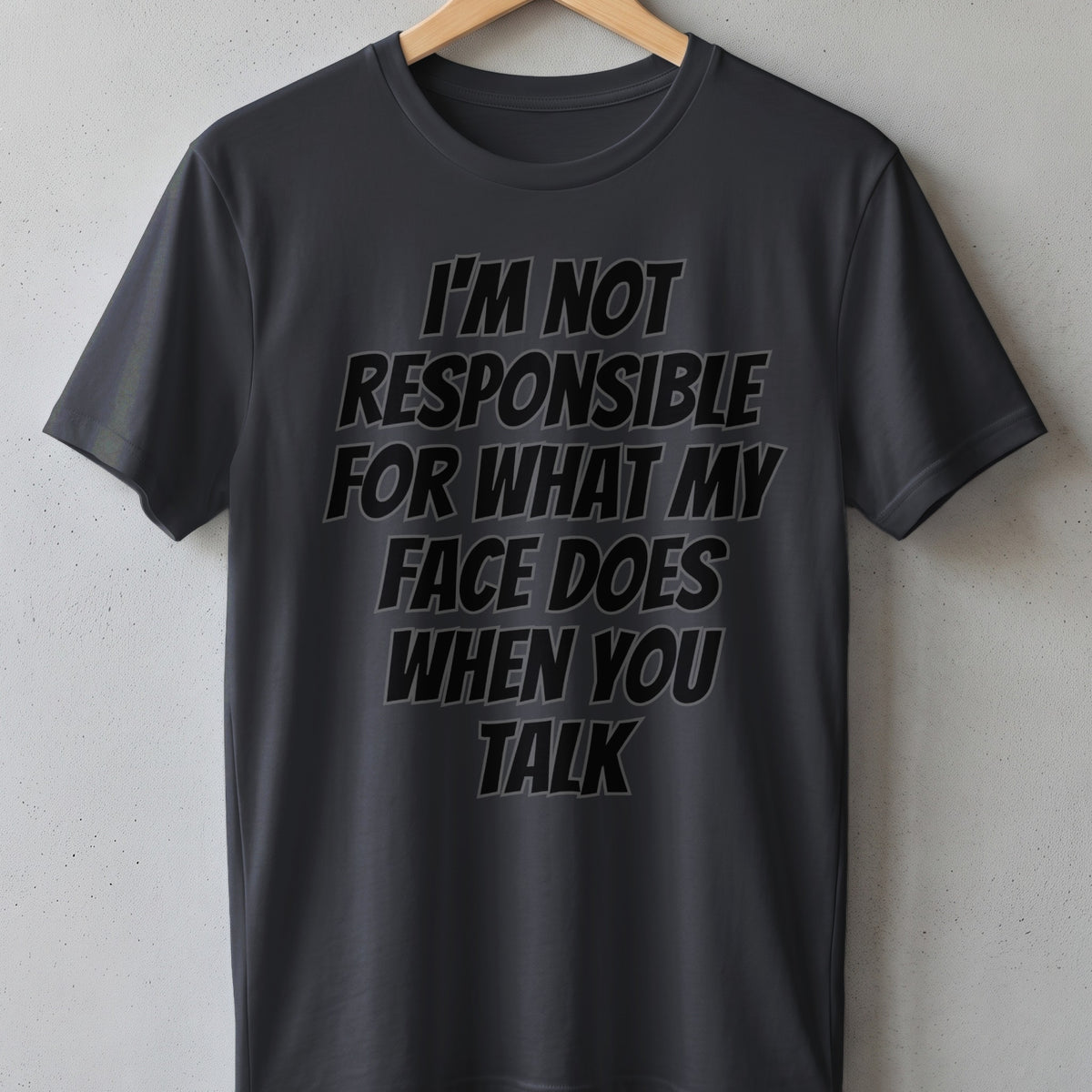 Dark grey t-shirt with black text reading "I'M NOT RESPONSIBLE FOR WHAT MY FACE DOES WHEN YOU TALK".