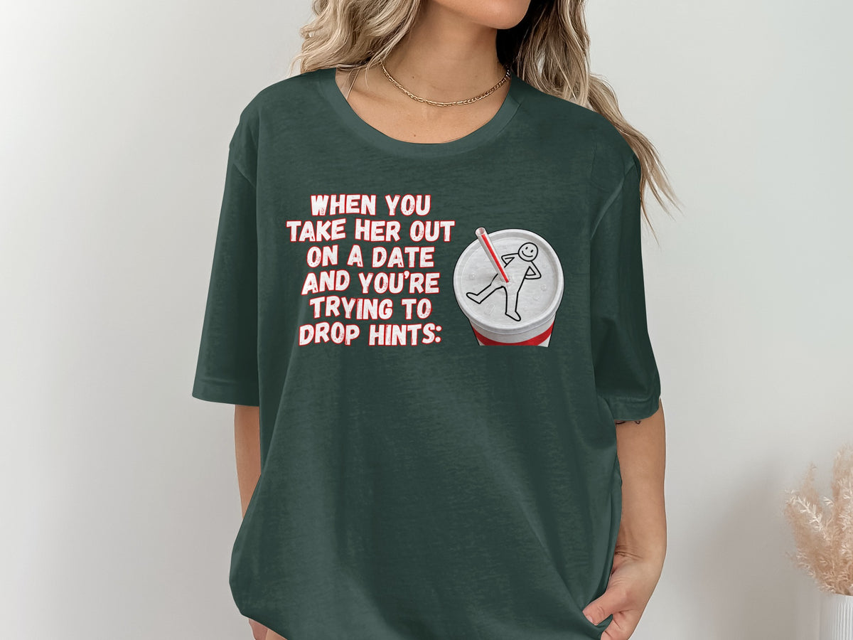 Dark green t-shirt with text "When you take her out on a date and you're trying to drop hints:" and a stick figure in a drink.