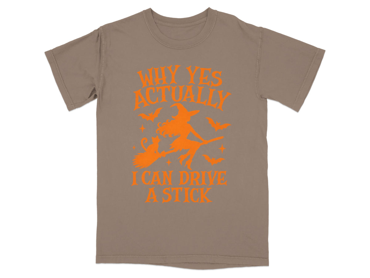Taupe t-shirt with orange graphic "Why Yes Actually I Can Drive A Stick" and witch.