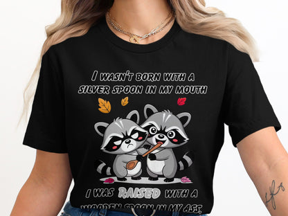 Two raccoons on a black t-shirt, one holding a spoon to the other's mouth.
