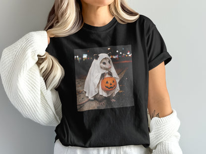 Opossum in ghost costume holding a carved pumpkin on a black t-shirt.