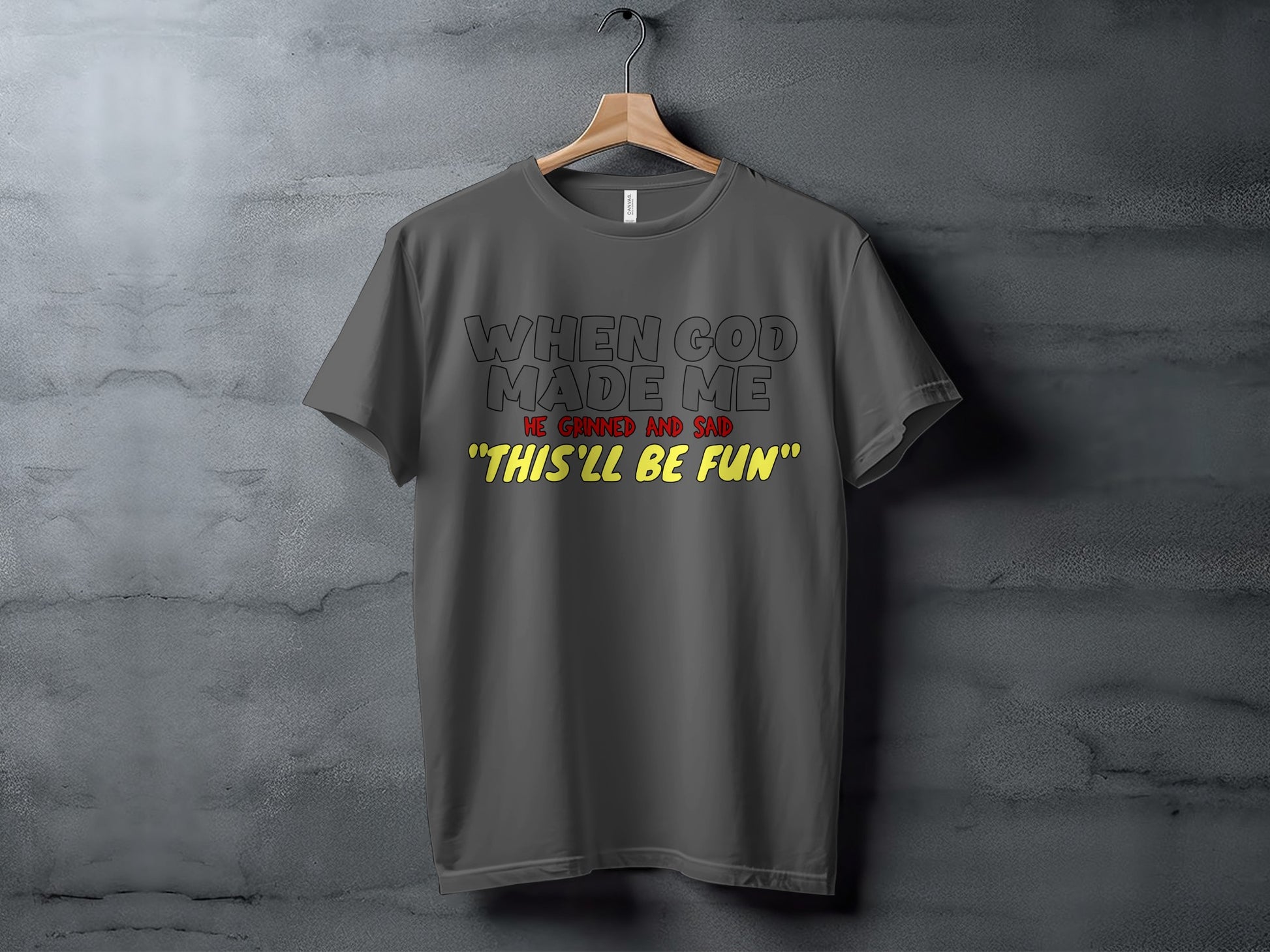 Dark grey t-shirt with black text "When God Made Me" and yellow text "This'll be fun".