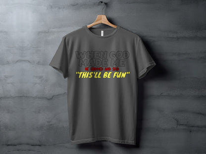 Dark grey t-shirt with black text "When God Made Me" and yellow text "This'll be fun".