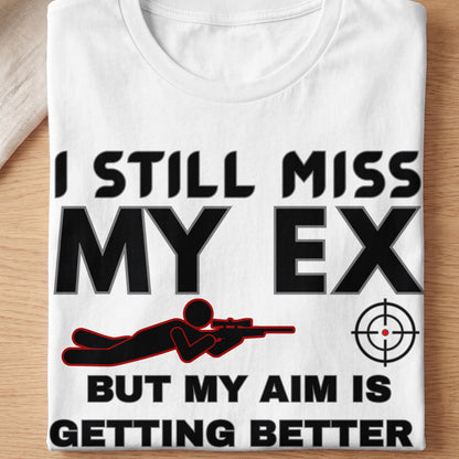 White t-shirt with text "I STILL MISS MY EX BUT MY AIM IS GETTING BETTER" and graphics.
