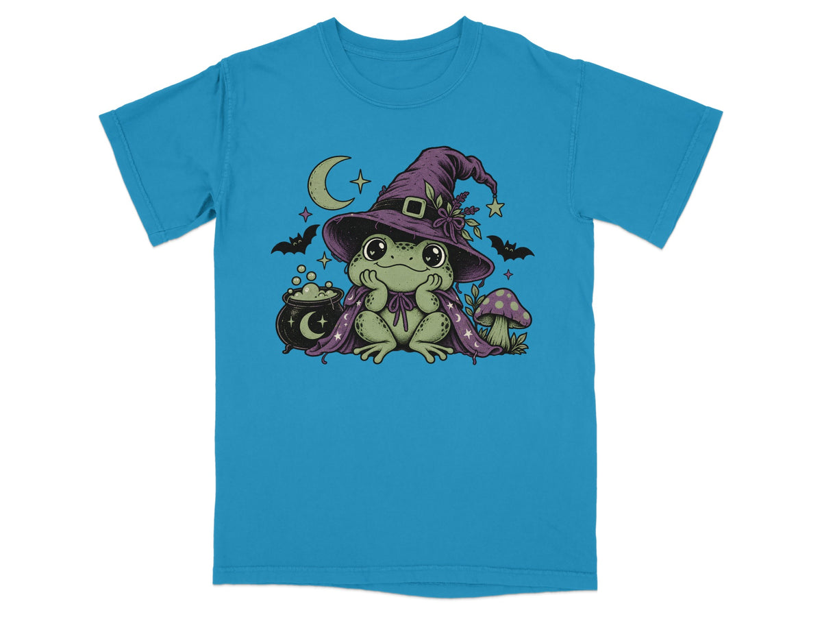 A bright blue t-shirt printed with a cute green frog wearing a witch hat and cape.