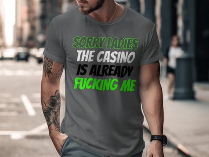 Man wearing a gray t-shirt with text "SORRY LADIES THE CASINO IS ALREADY FUCKING ME".
