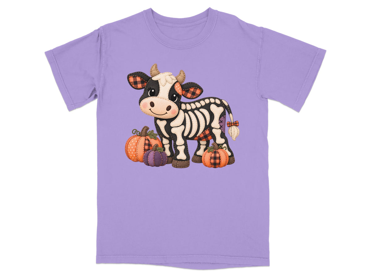 Skeleton cow with plaid accents and pumpkins on a light purple t-shirt.