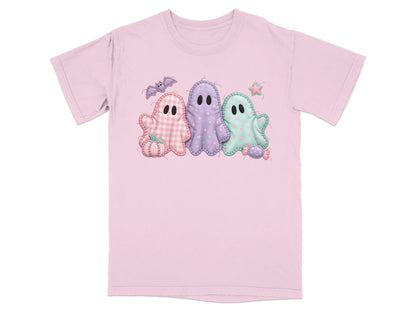 Three pastel Halloween ghosts with pumpkin, bat, and candy decorations on pink t-shirt.