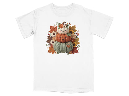 Three smiling knit pumpkins stacked with fall leaves and flowers.