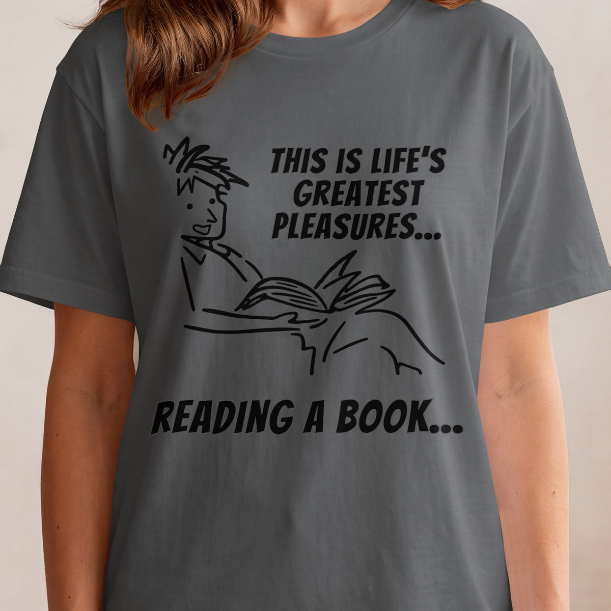 T-shirt graphic: cartoon of person reading, text "THIS IS LIFE'S GREATEST PLEASURES... READING A BOOK..."
