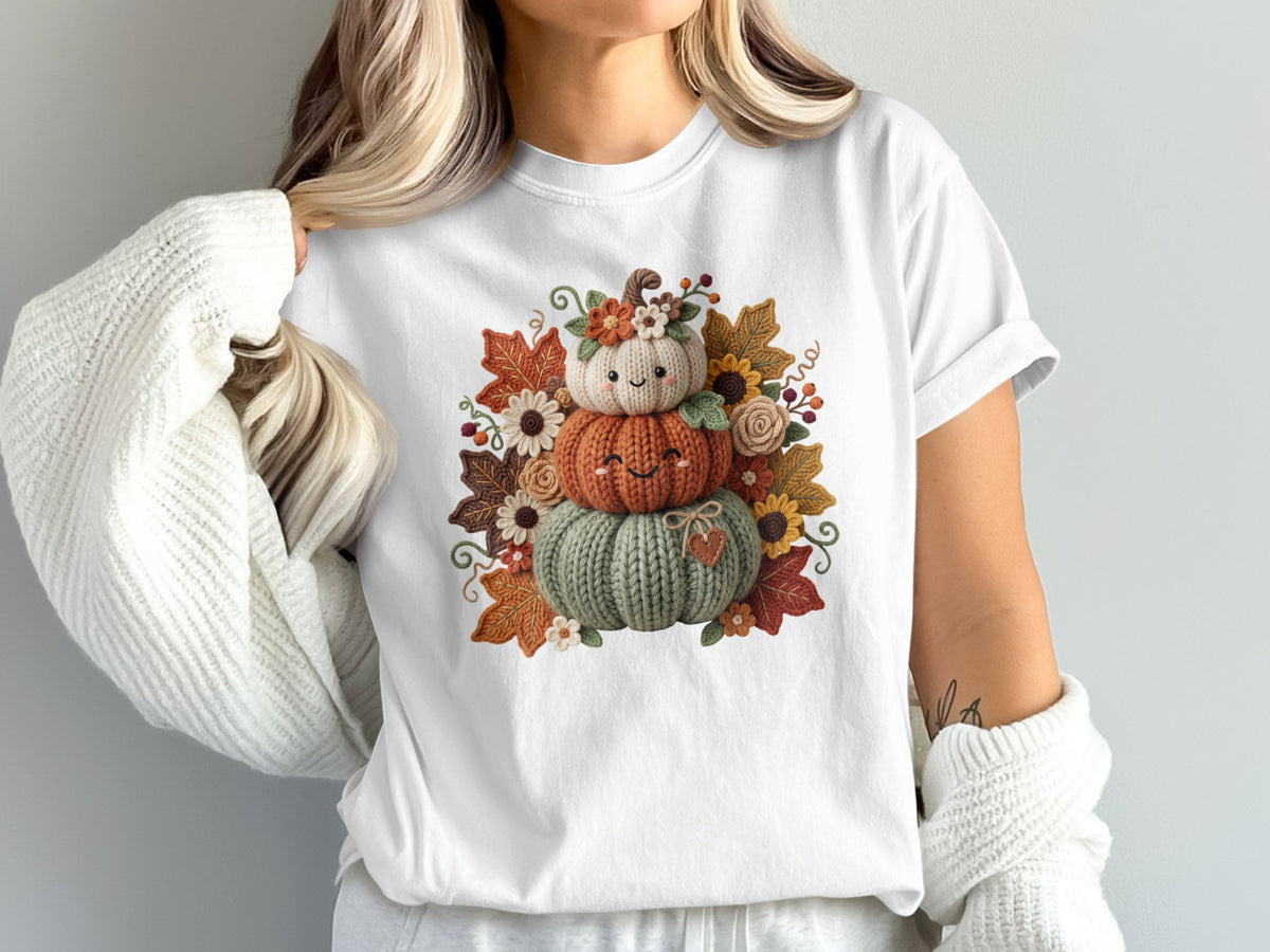 White t-shirt with stacked knitted pumpkins and autumn leaves graphic.