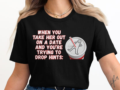 Black t-shirt with text "When you take her out on a date and you're trying to drop hints" and a drawing of a body outline on a cup.