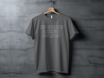 Dark grey t-shirt with white text that reads "THIS ADULT SHIT STARTING TO PISS ME OFF".