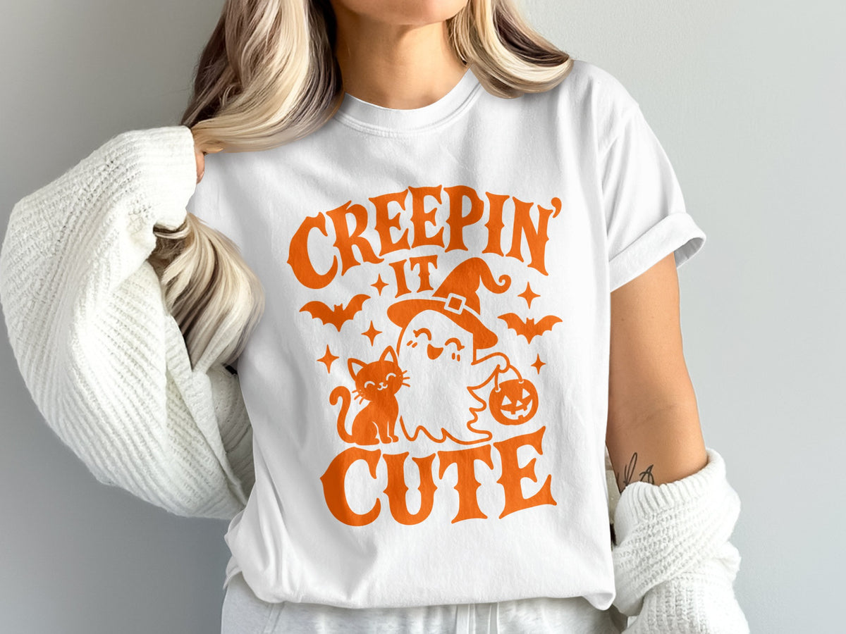 White t-shirt with orange graphic "CREEPIN' IT CUTE" featuring a ghost, cat, bats, and pumpkin.