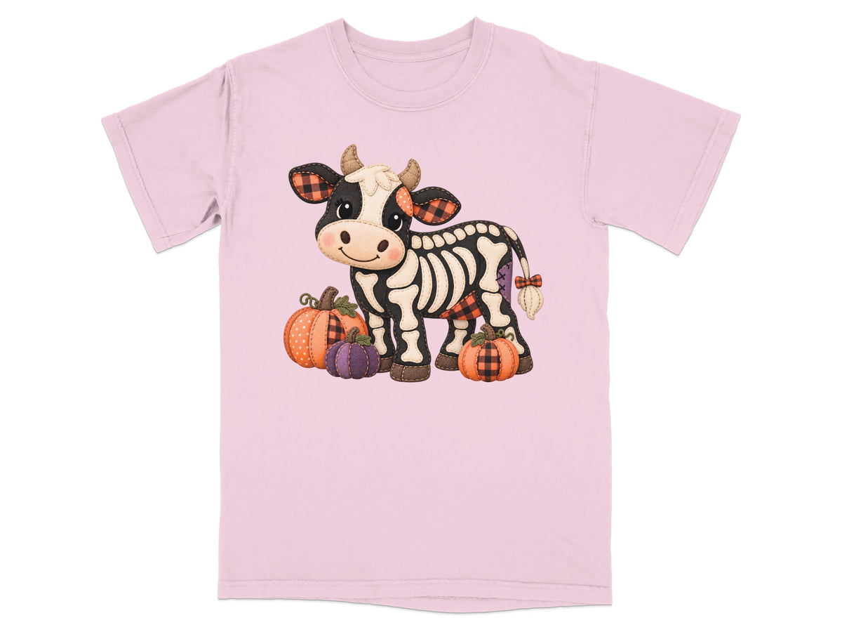 Skeleton cow with pumpkins and buffalo plaid accents on a pink t-shirt.