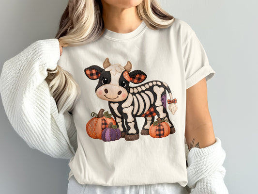 Skeleton cow with pumpkins and plaid details on a white t-shirt.