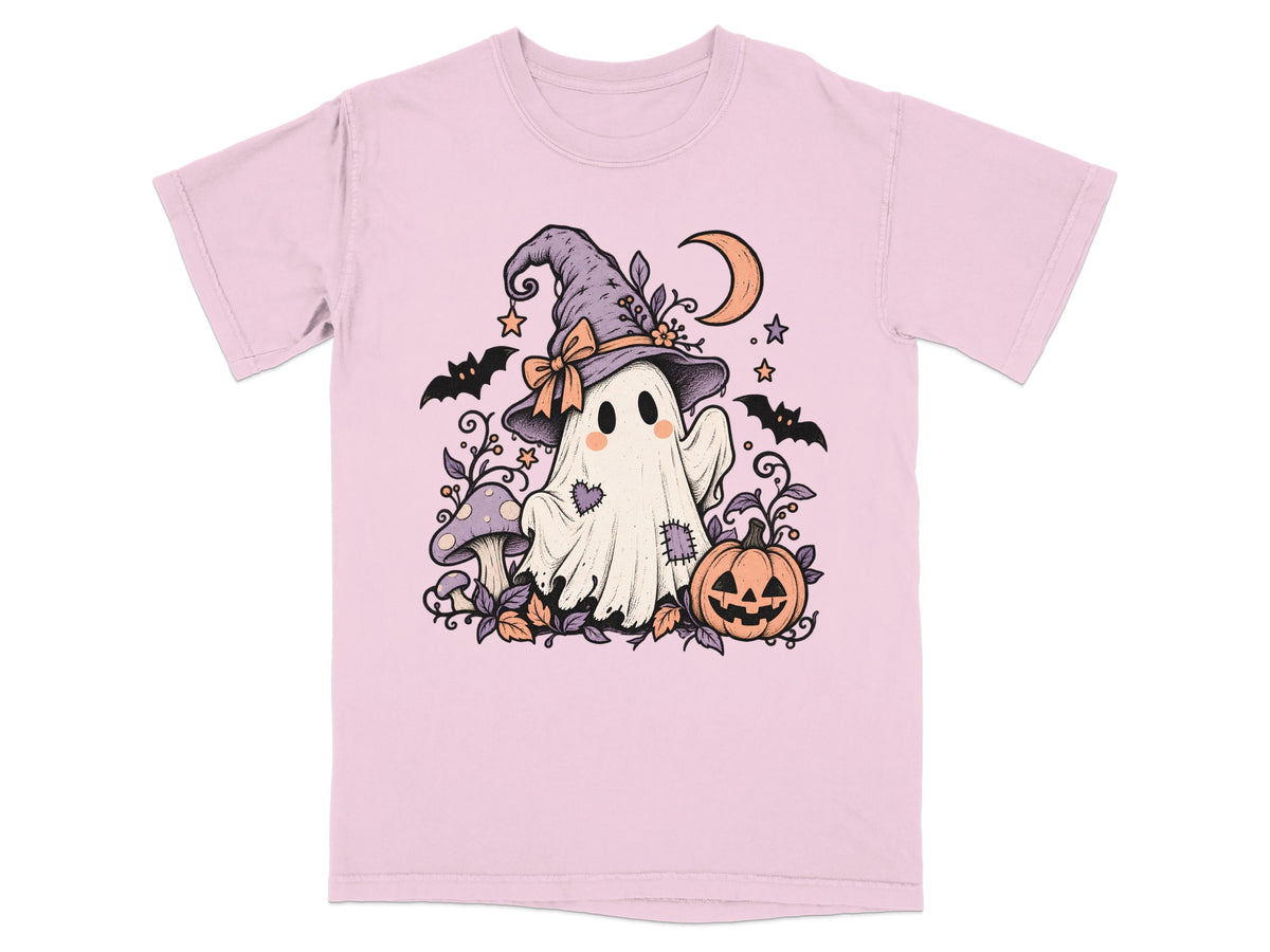 A light pink t-shirt featuring an illustration of a cute ghost wearing a witch hat, surrounded by bats, pumpkins, and mushrooms.