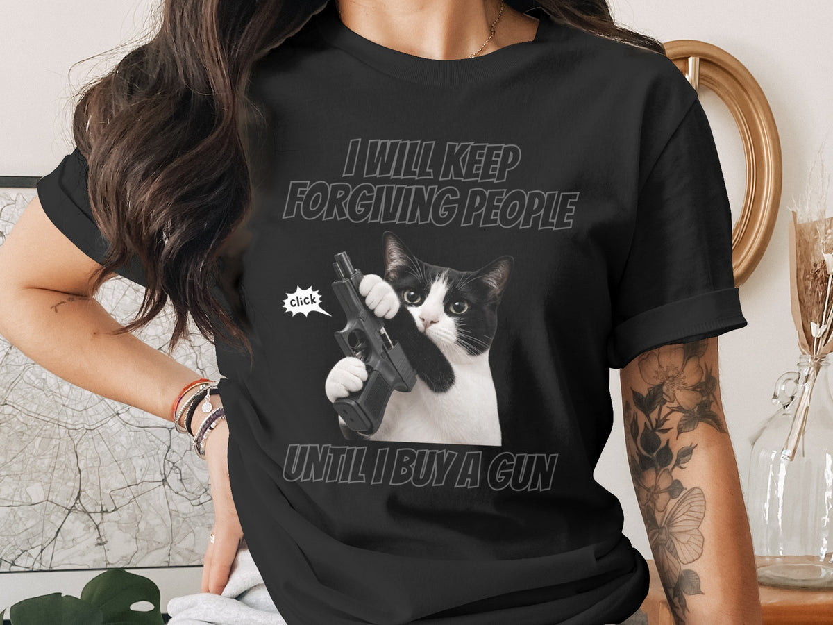 Black t-shirt with a cat holding a gun and text "I WILL KEEP FORGIVING PEOPLE UNTIL I BUY A GUN".