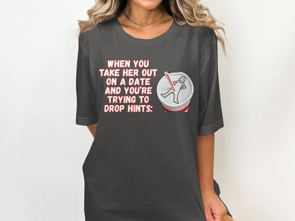 Dark t-shirt with "When you take her out on a date and you're trying to drop hints:" text and a soda cup graphic.
