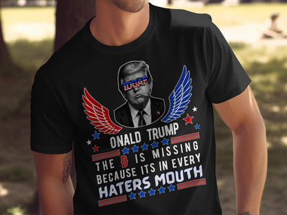 Black t-shirt featuring Donald Trump with American flag glasses and wings, text reads "ONALD TRUMP THE D IS MISSING BECAUSE ITS IN EVERY HATERS MOUTH".
