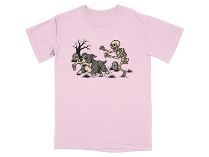 A light pink t-shirt featuring a cartoon graphic of a skeleton chasing a dog holding a bone.