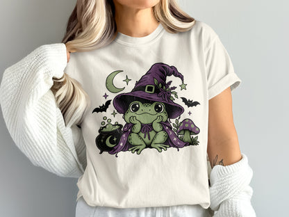 A woman wearing a white t-shirt featuring a green frog wearing a witch hat and cape.