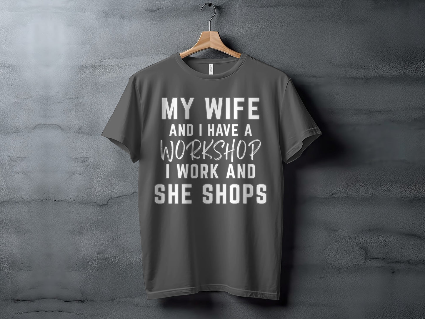 Dark grey t-shirt with text: "MY WIFE AND I HAVE A WORKSHOP I WORK AND SHE SHOPS".