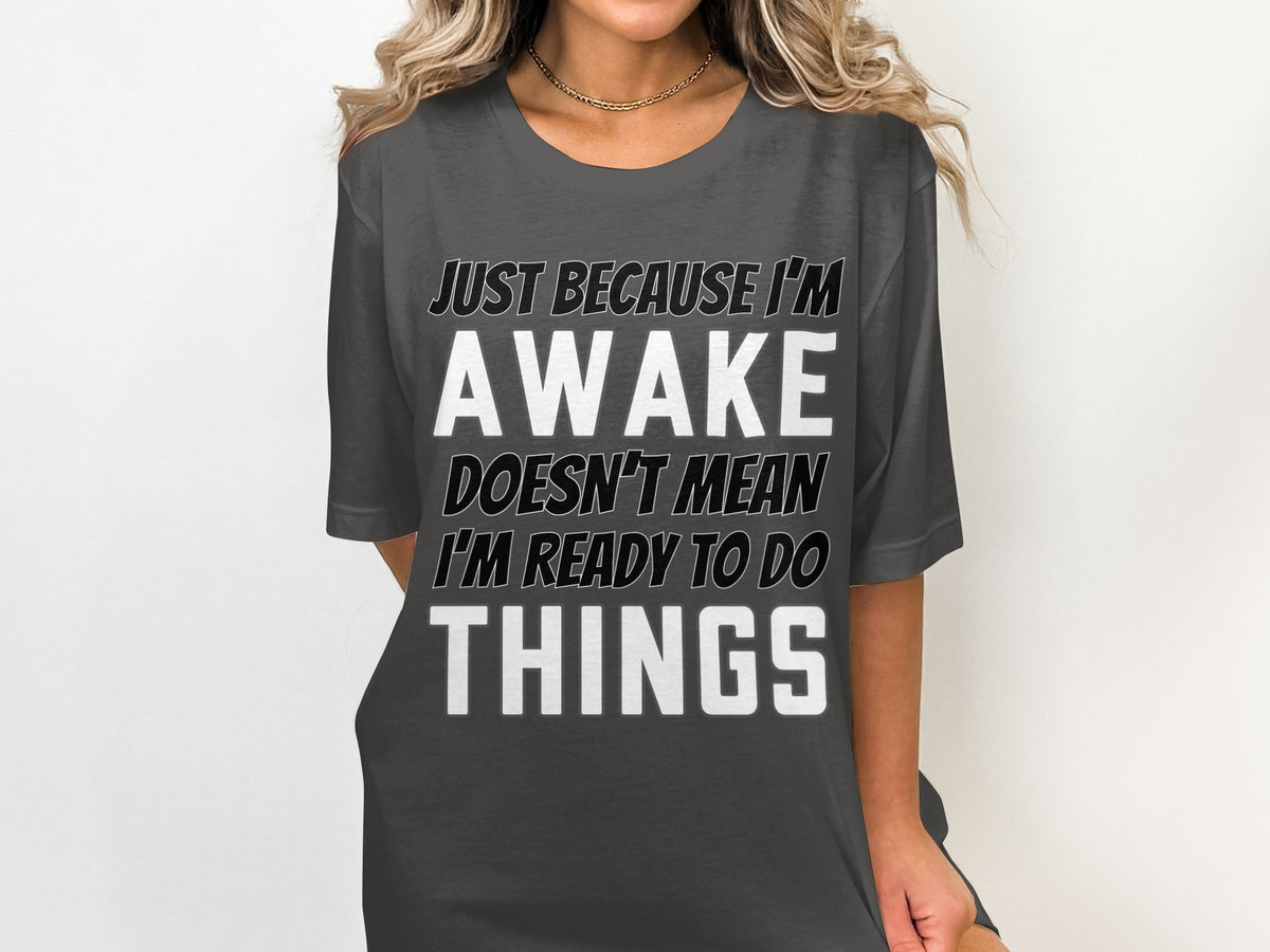 Dark grey t-shirt with text that reads "JUST BECAUSE I'M AWAKE DOESN'T MEAN I'M READY TO DO THINGS".