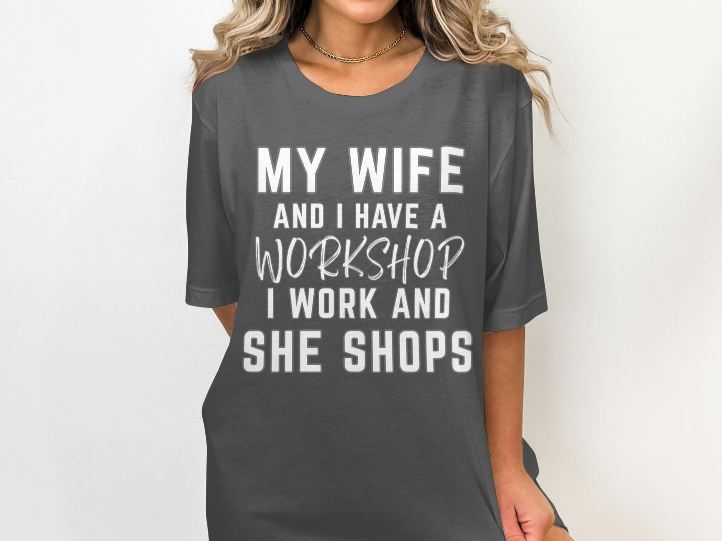 Dark grey t-shirt with white text: My wife and I have a workshop. I work and she shops.
