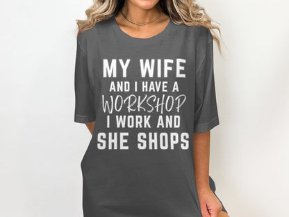 Dark grey t-shirt with white text: My wife and I have a workshop. I work and she shops.