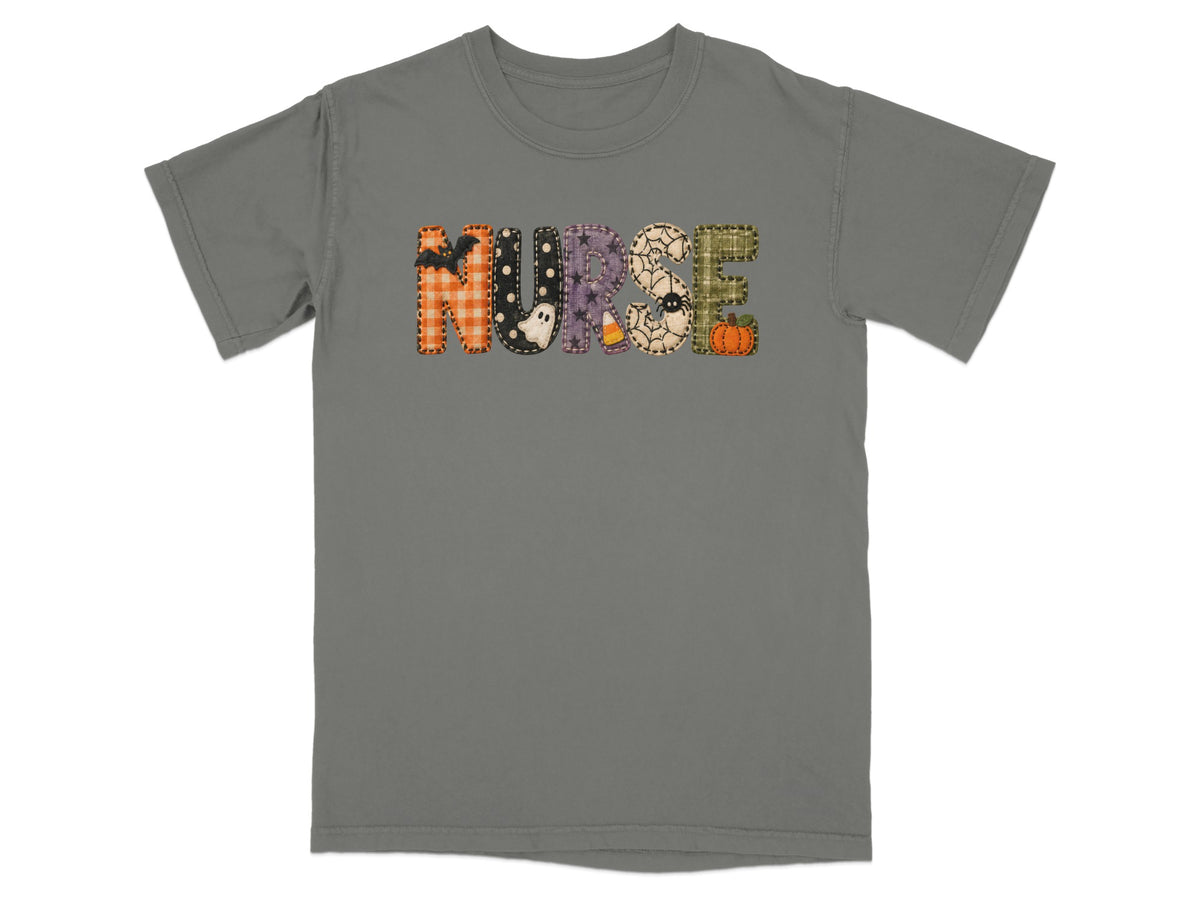 A grey short-sleeve t-shirt with the word NURSE spelled out in patterned Halloween-themed letters across the chest.