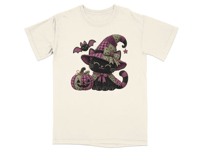 An off-white short-sleeve t-shirt with a graphic of a black cat wearing a purple witch hat, sitting next to a jack-o-lantern.