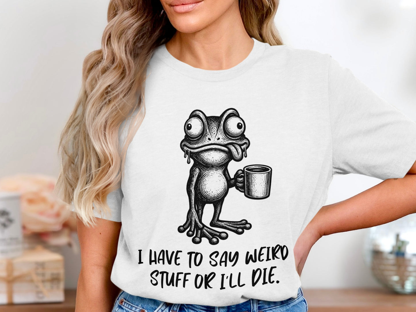 White t-shirt with a cartoon frog holding a mug and the text "I HAVE TO SAY WEIRD STUFF OR I'LL DIE."