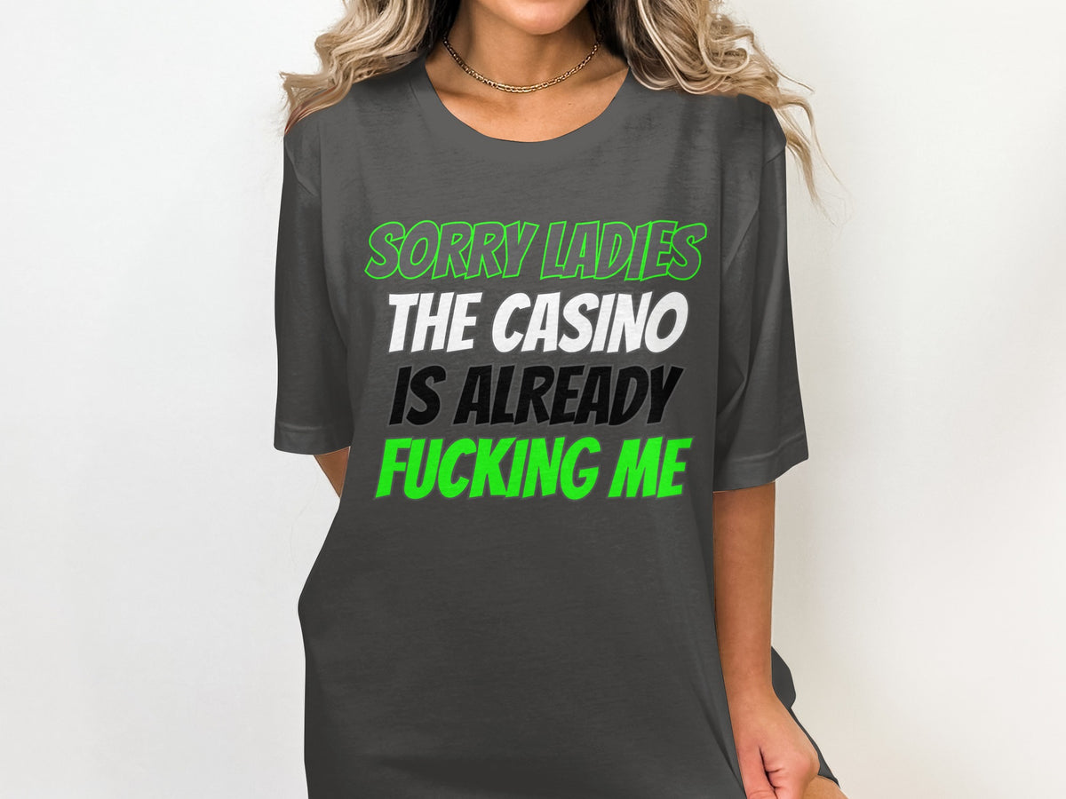 Dark grey t-shirt with text: "SORRY LADIES THE CASINO IS ALREADY FUCKING ME."
