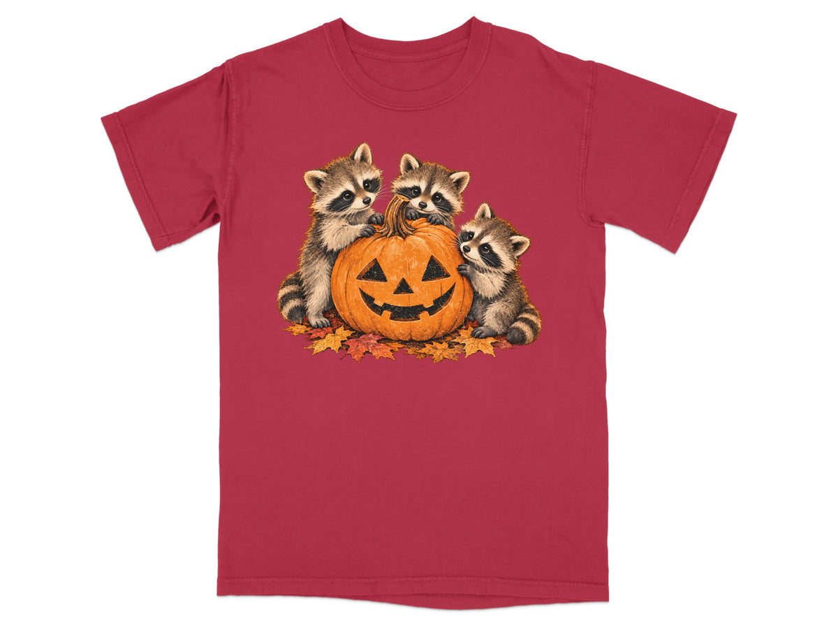Three raccoons interacting with a carved pumpkin on a bed of fall leaves.