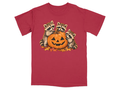 Three raccoons interacting with a carved pumpkin on a bed of fall leaves.