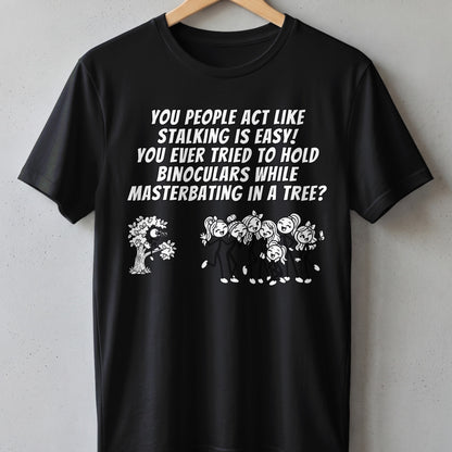 Black t-shirt with text and illustration of a figure in a tree observing people.