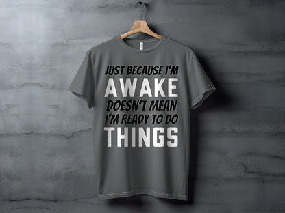 Gray t-shirt with text "JUST BECAUSE I'M AWAKE DOESN'T MEAN I'M READY TO DO THINGS".