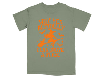 Olive green t-shirt with orange Halloween graphic and text reading "Why Yes Actually I Can Drive A Stick"