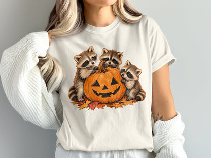 Three raccoons sit with a jack-o'-lantern surrounded by autumn leaves.