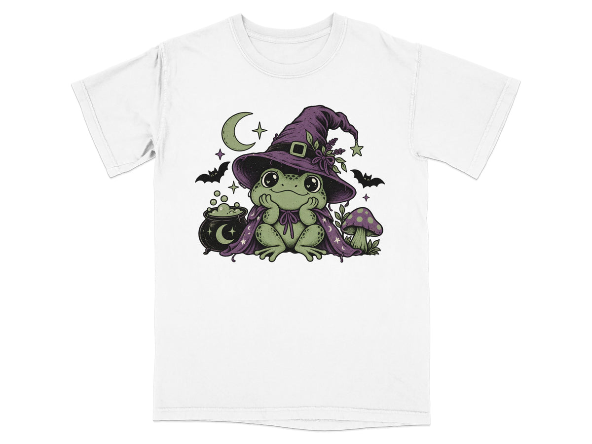 A white t-shirt featuring a graphic of a cute green frog wearing a witch hat and cape.