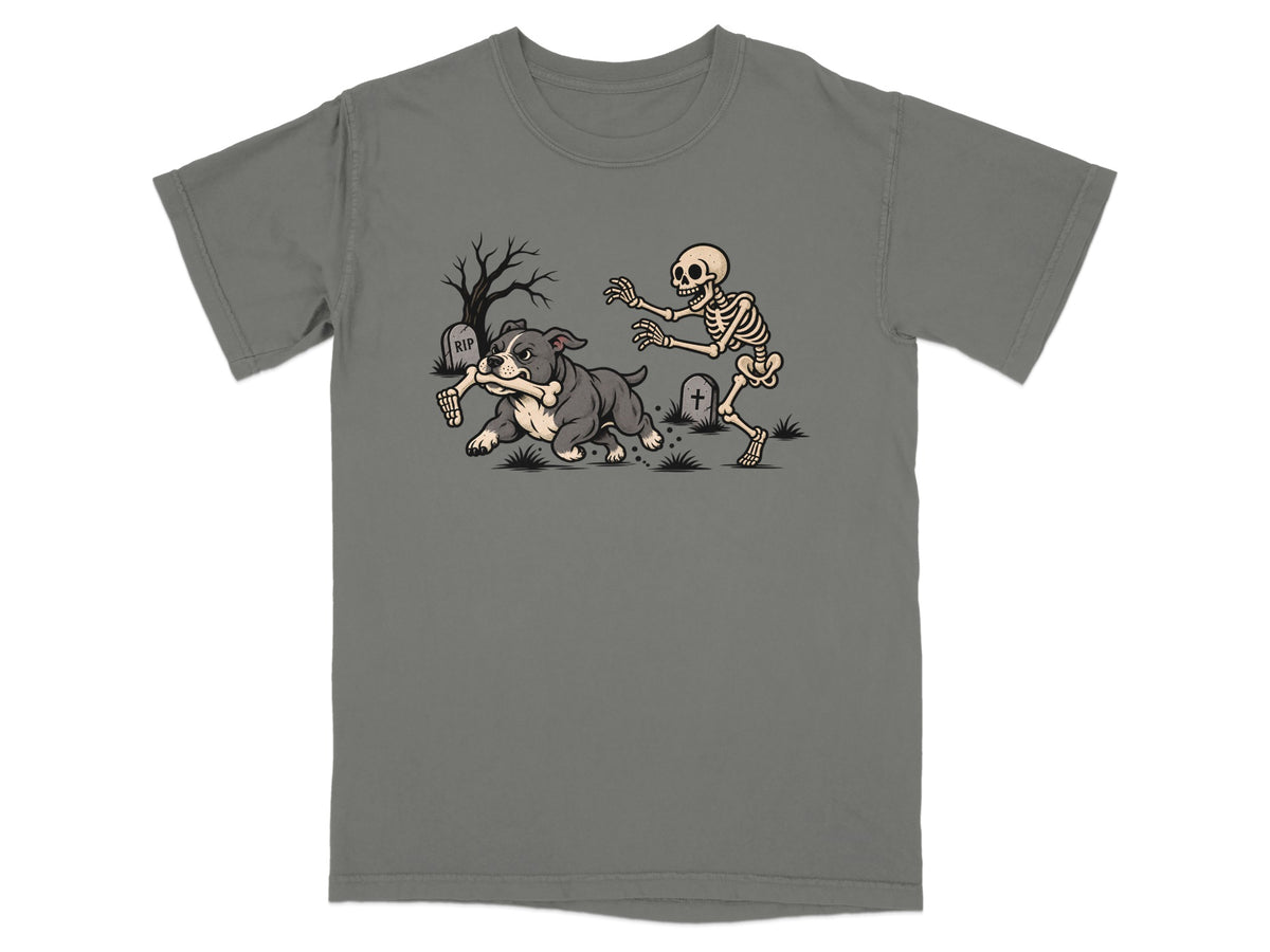 A grey t-shirt featuring a graphic of a skeleton chasing a bulldog holding a bone in a graveyard.