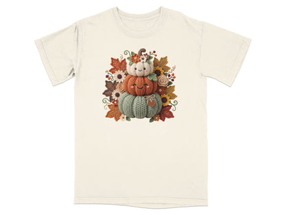 Stack of three smiling knitted pumpkins surrounded by autumn leaves and flowers.